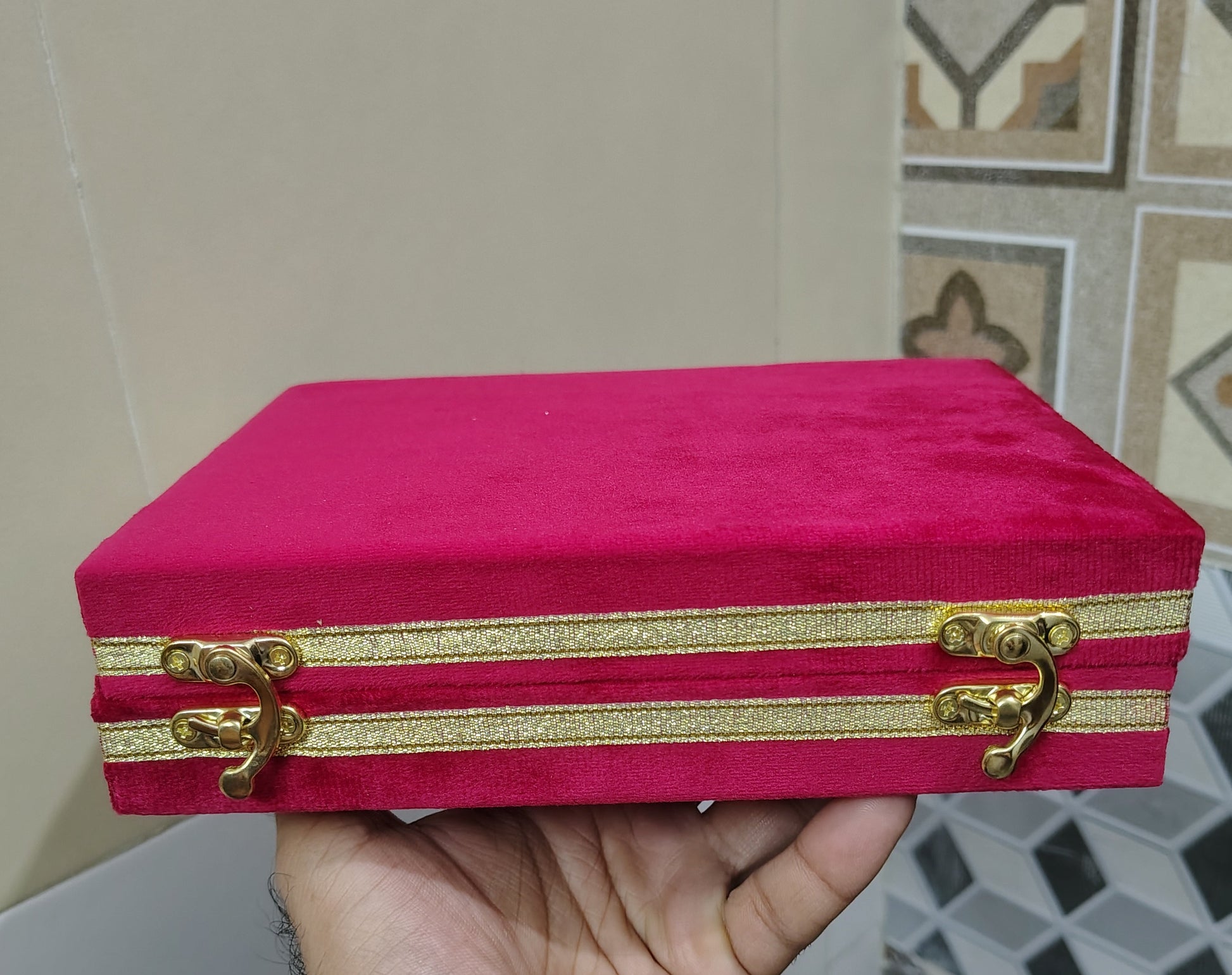 Hand holding a red box with gold accents against a tiled wall background